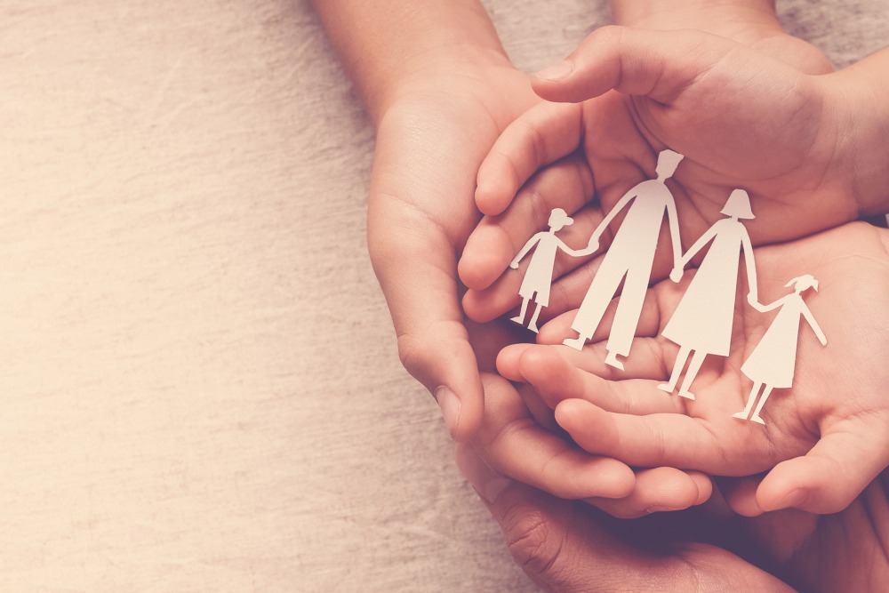 Two sets of hands cupped together holding a paper cutout of a family