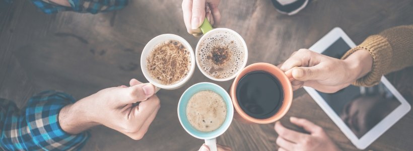 Four hands placing four coffee cups together