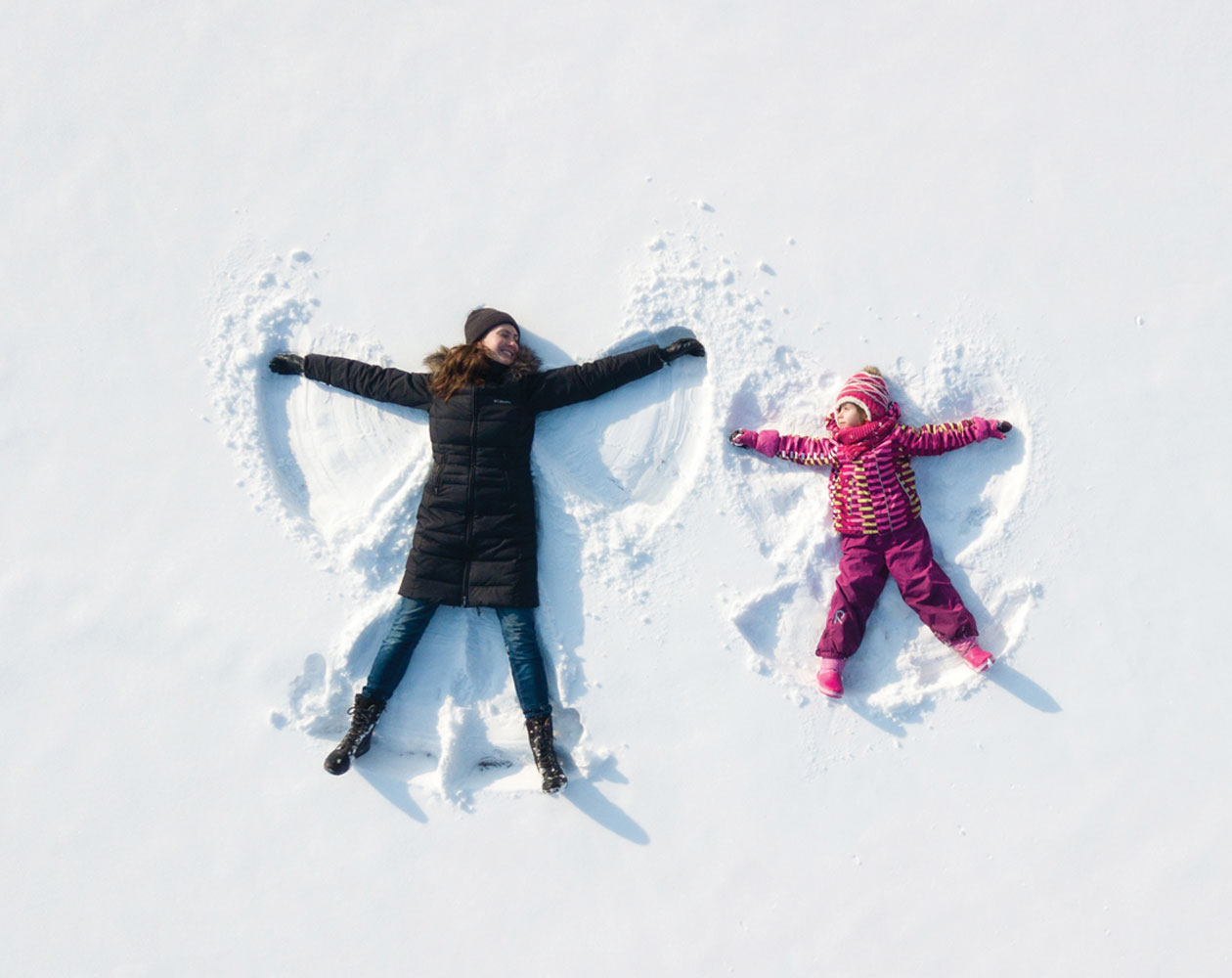 A mother and her child making snow angels in the snow